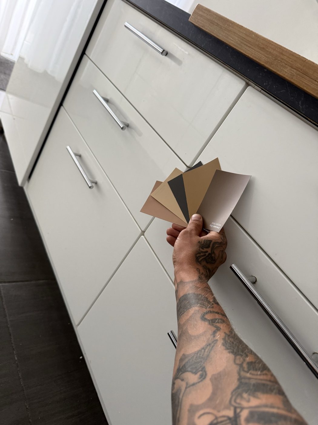 Staalkaarten met foliekleuren worden naast een bestaande witte keuken gehouden om de nieuwe kleur te kiezen